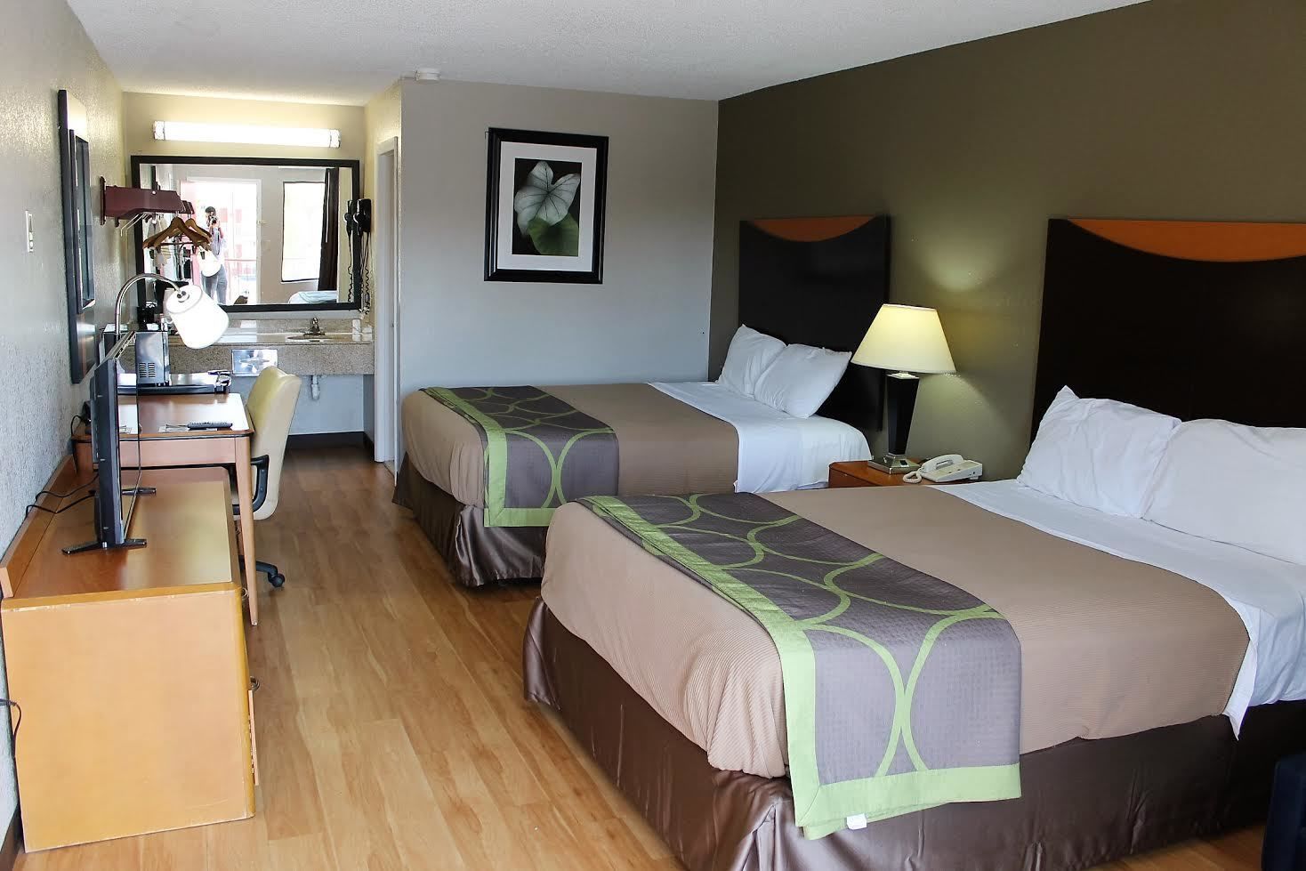 Habitación de hotel con dos camas, un escritorio, una silla, un espejo y un cuadro en la pared.