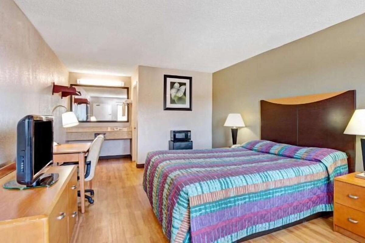Una habitación de hotel con cama, escritorio, silla, televisor y una pequeña kitchenette.