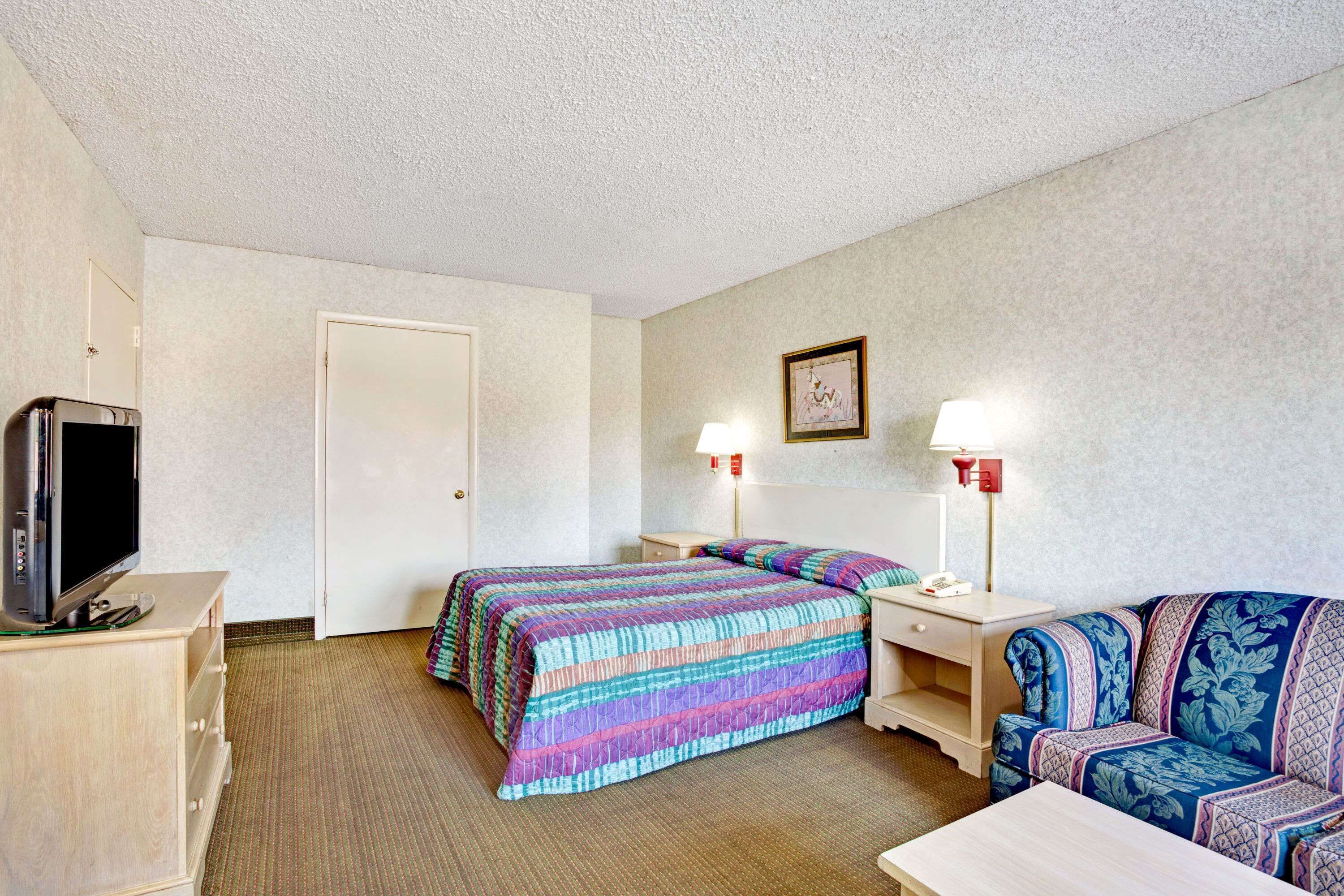A hotel room with a bed, a sofa, a TV, and two bedside lamps.