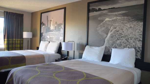 A hotel room with two beds, a cityscape painting, and a beach scene painting on the wall.