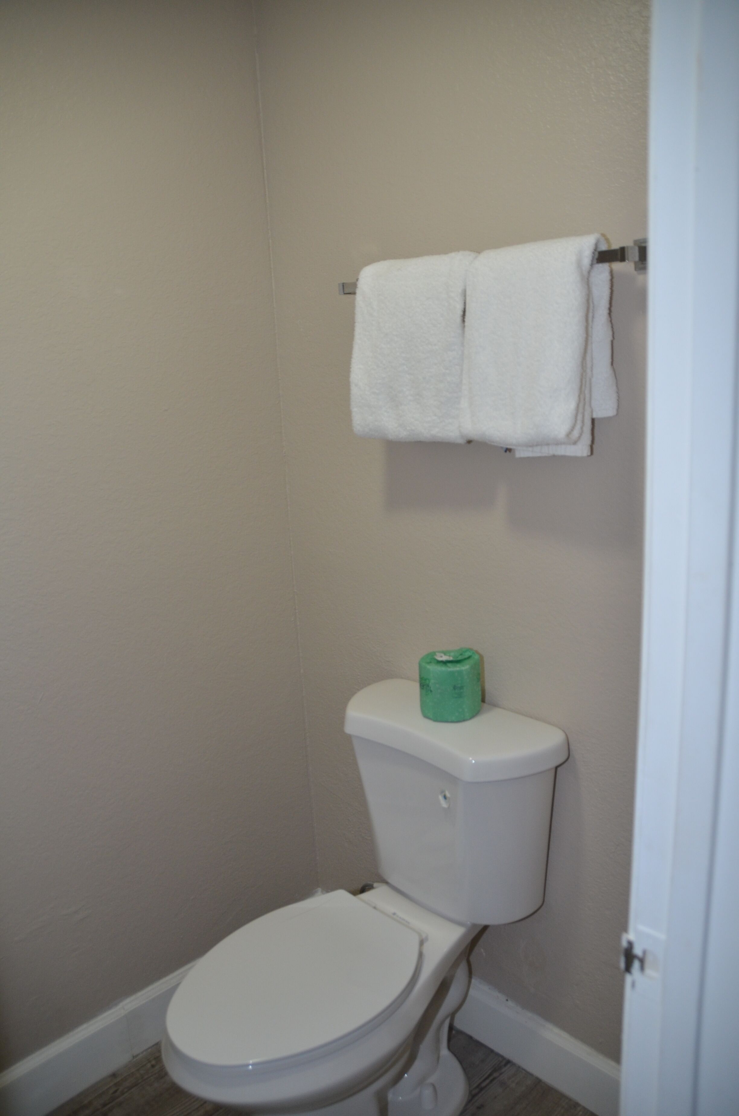 Ein kleines, sauberes Badezimmer mit einer weißen Toilette, einem grünen Toilettenpapierhalter und einem weißen Handtuch, das an einem Haken hängt.