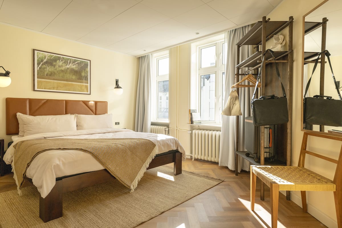 A bedroom with a bed, a wooden chair, a radiator, and a window with curtains.