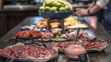 Un buffet proposant une variété de viandes, de fruits et un distributeur de boissons.