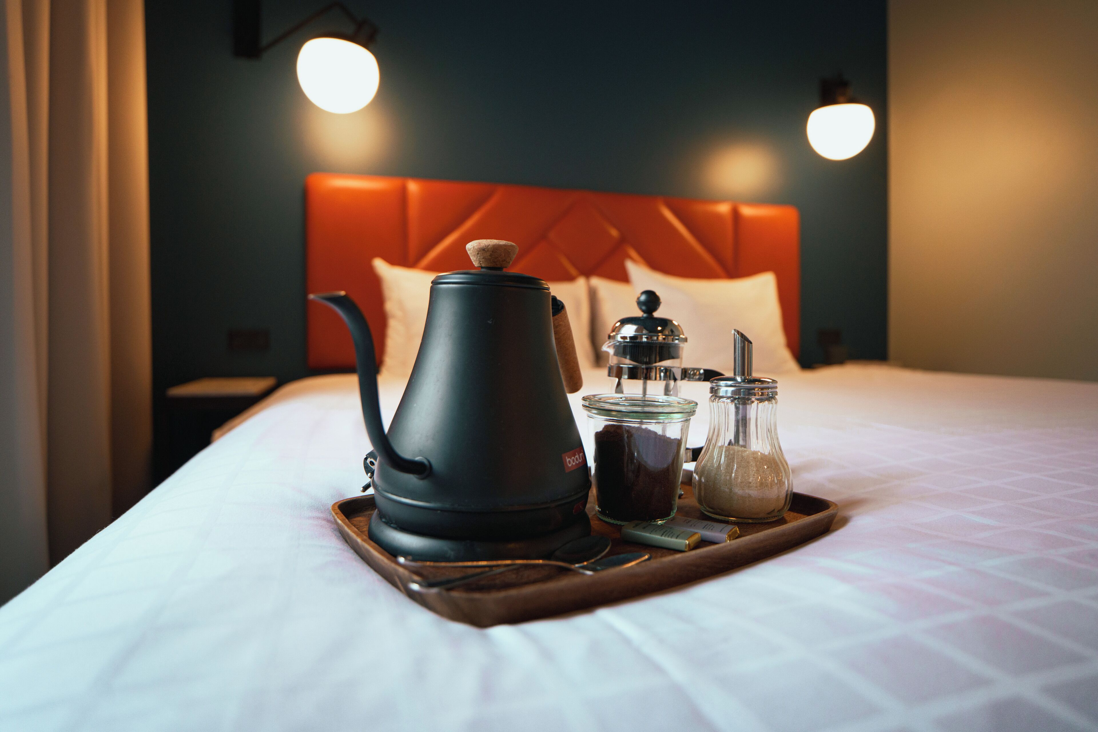 A bed with a tray containing a coffee maker, a glass jar, and a salt shaker.
