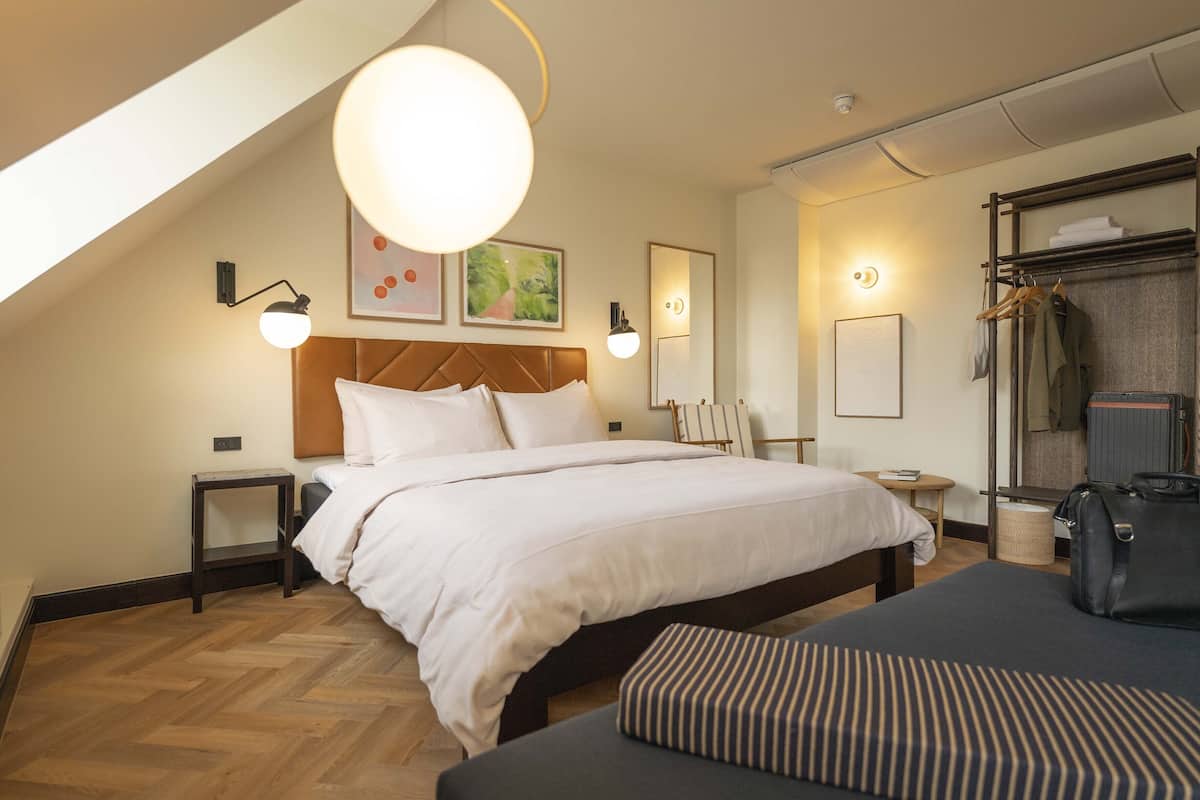 A bedroom with a large bed, a bedside table, a hanging light fixture, a wardrobe, and a suitcase.