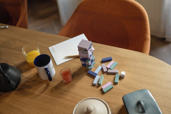 Una mesa de madera con una pila de bloques de colores, una taza blanca, un vaso de jugo de naranja, una tetera negra y una tetera blanca.