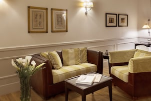 A living room with a brown leather sofa, a green armchair, a coffee table with books, and framed artwork on the wall.