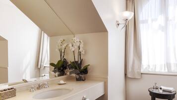 A bathroom with a double sink, a mirror, a small table with toiletries, and orchid flowers on the wall.