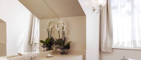 A bathroom with a double sink, a mirror, a small table with toiletries, and orchid flowers on the wall.