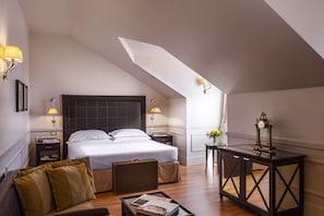 Habitación de hotel con cama, mesita de noche, lámpara, una pequeña mesa con bandeja, sofá y un reloj decorativo.