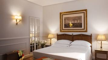 A hotel room with a large bed, two bedside lamps, a framed historical painting, a door with glass panels, and a suitcase on the floor.