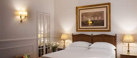 A hotel room with a large bed, two bedside lamps, a framed historical painting, a door with glass panels, and a suitcase on the floor.