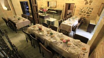 Un restaurant doté de nombreuses tables dressées pour le service, de murs en pierre et d’un décor intérieur rustique.