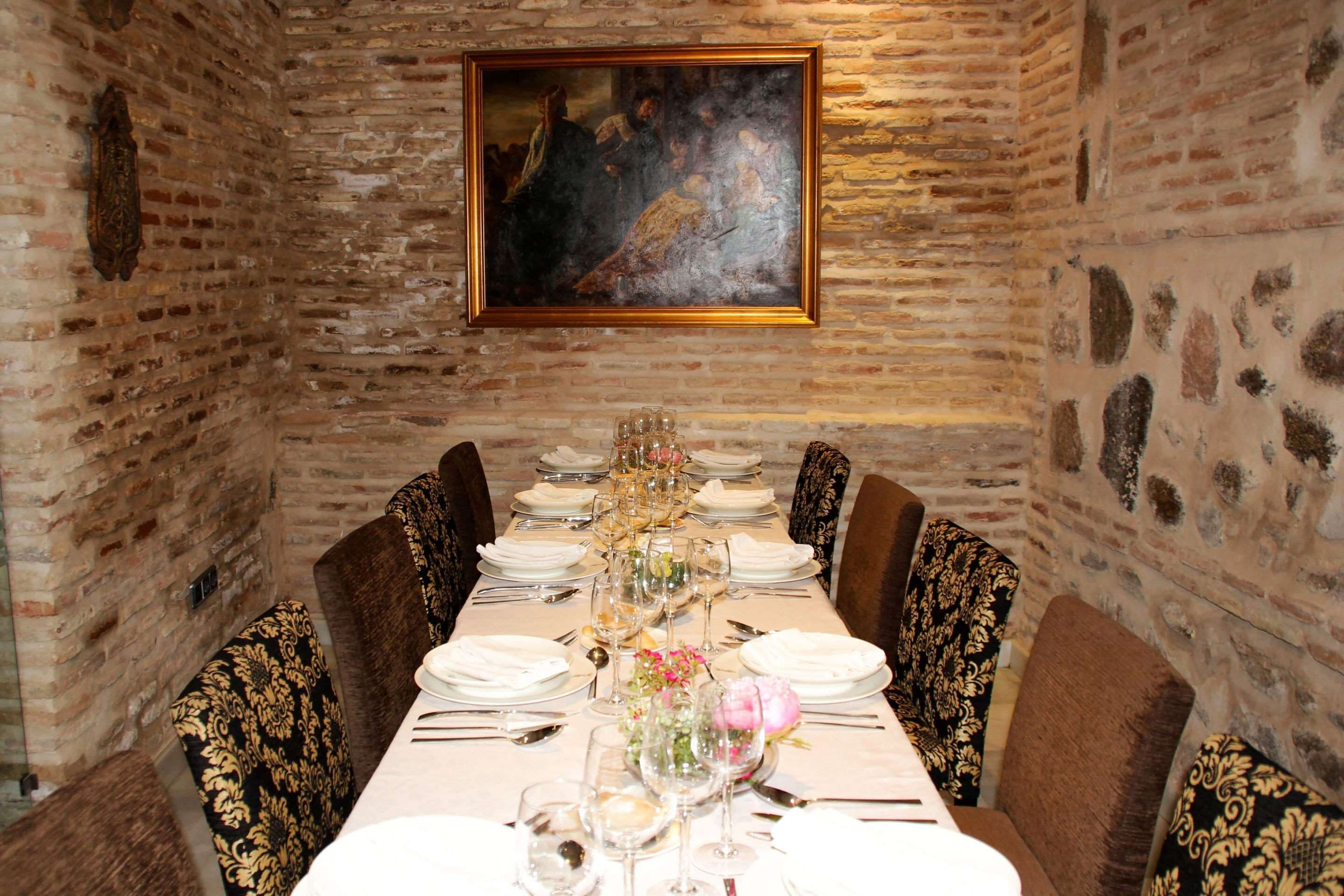 A long dining table set for a meal in a room with brick walls and a framed painting above.