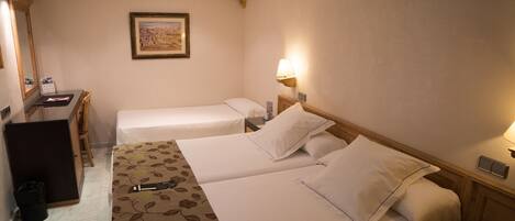 A hotel room with two single beds, a desk with a chair, a small trash bin, and a framed picture on the wall.