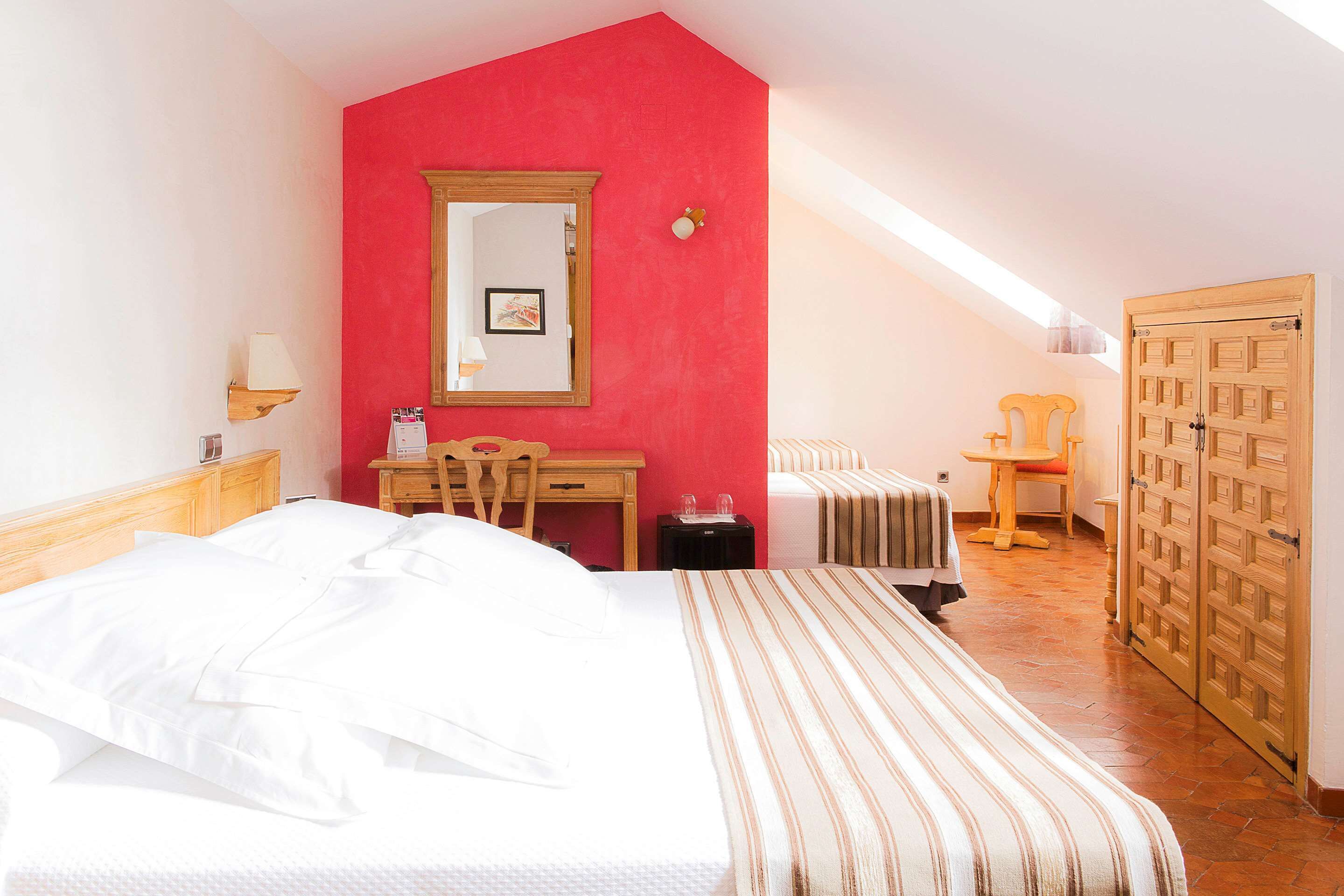 Una habitación de hotel con cama, escritorio, silla, armario y un espejo en la pared.