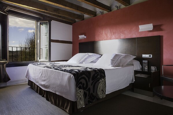 Habitación de hotel con una cama grande, una mesita de noche, una ventana con vistas y una pared de acento roja.