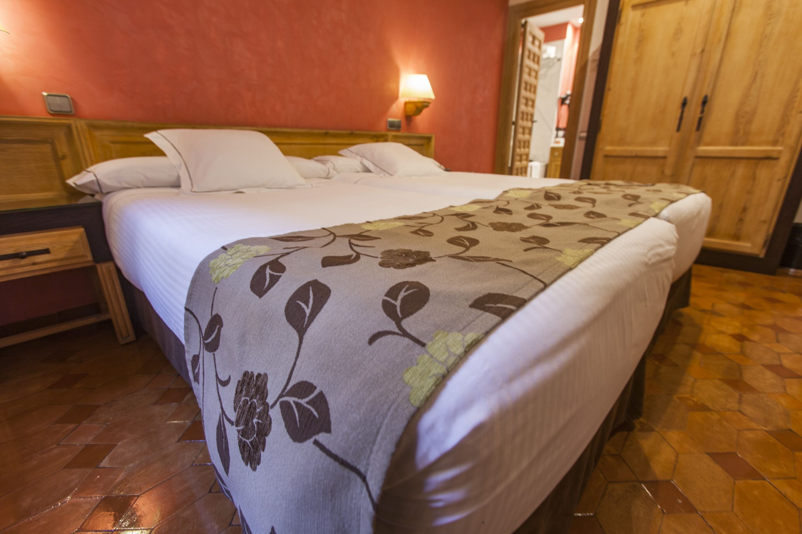 A hotel room with a bed, wooden headboard, a nightstand, a lamp, and a wardrobe.