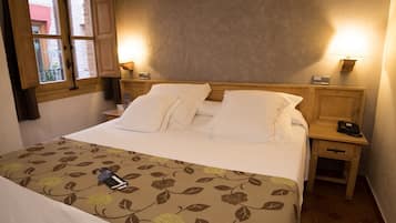 Una cama bien hecha con sábanas blancas, una colcha de estampado floral y una mesita de noche con una lámpara y un teléfono.