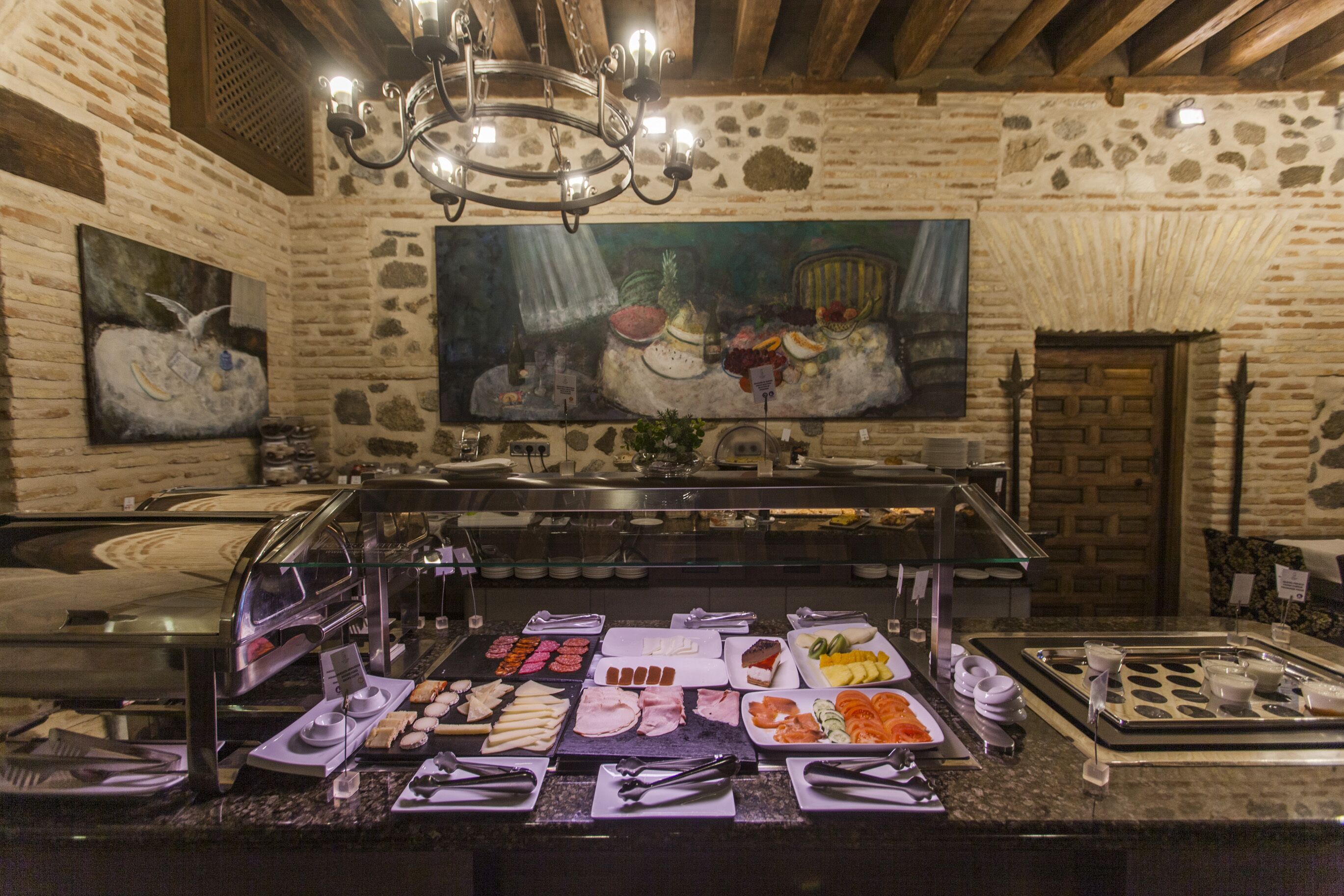 A buffet with various food items and a stone wall with artwork.