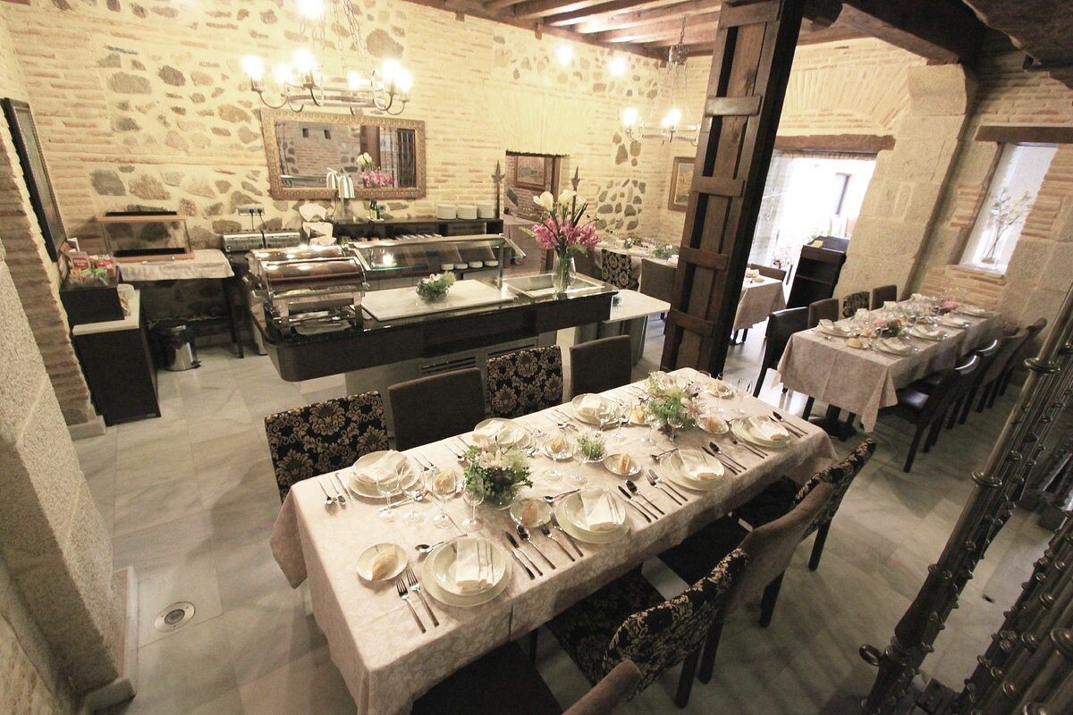 A restaurant with a stone wall interior, multiple dining tables set for service, and a chandelier.
