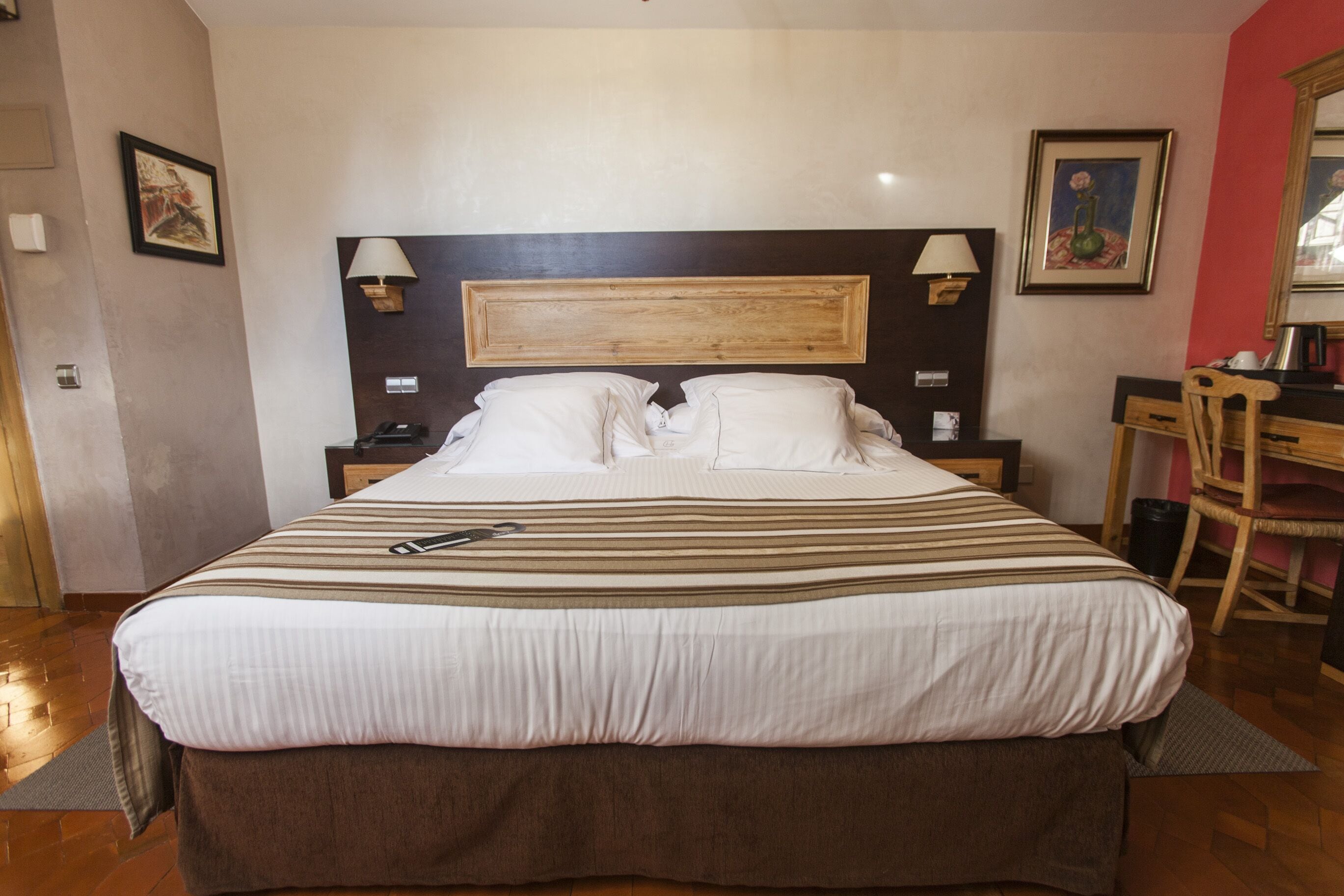 A neatly made bed with striped bedding, a wooden headboard, bedside lamps, and a desk with a chair in a hotel room.