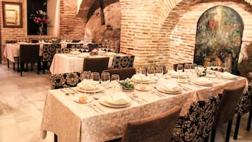 Un restaurante con paredes de ladrillo y techos abovedados, mesas dispuestas con manteles blancos y fundas de sillas estampadas con motivos florales.