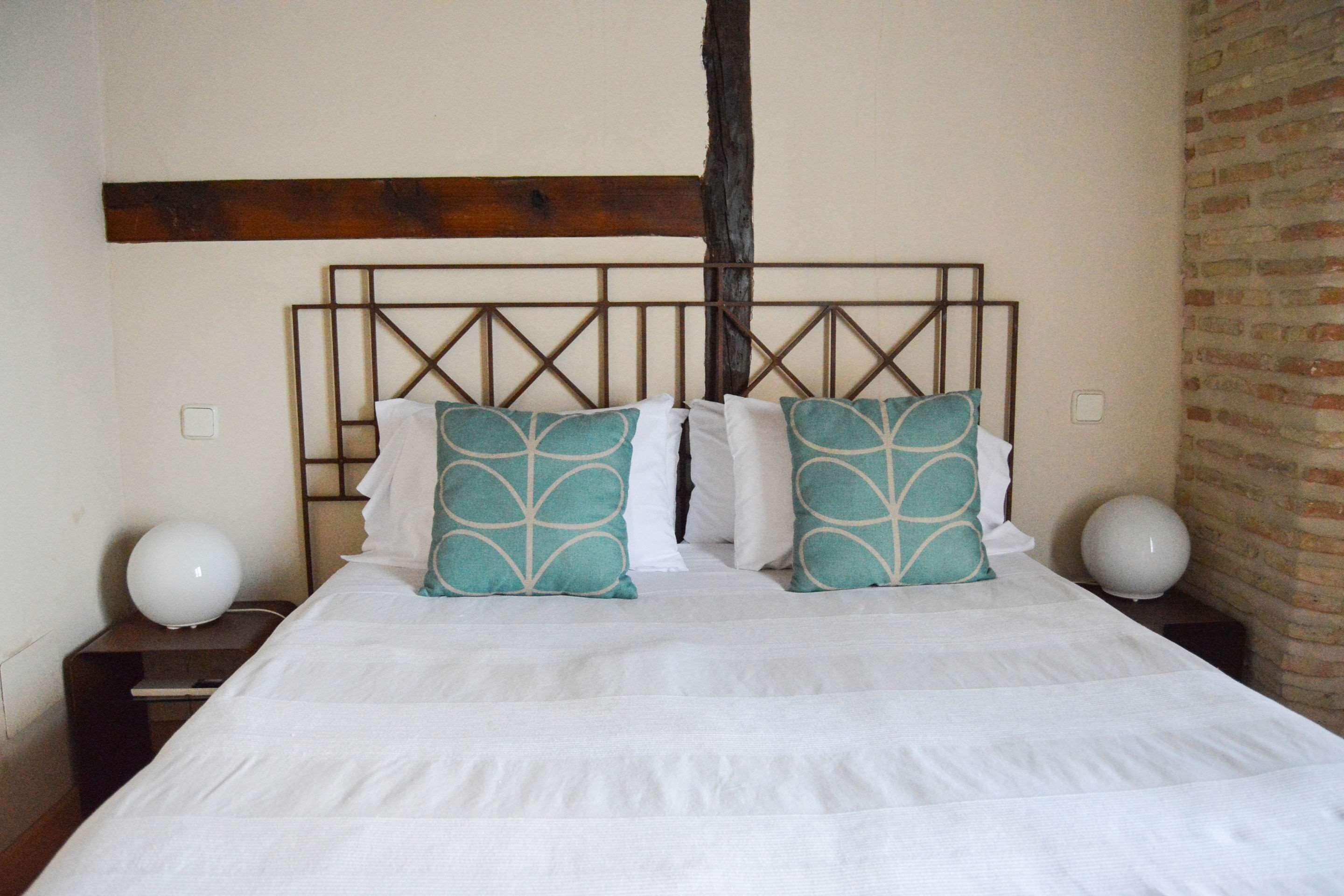 A bed with a wooden headboard, white bedding, and teal pillows.