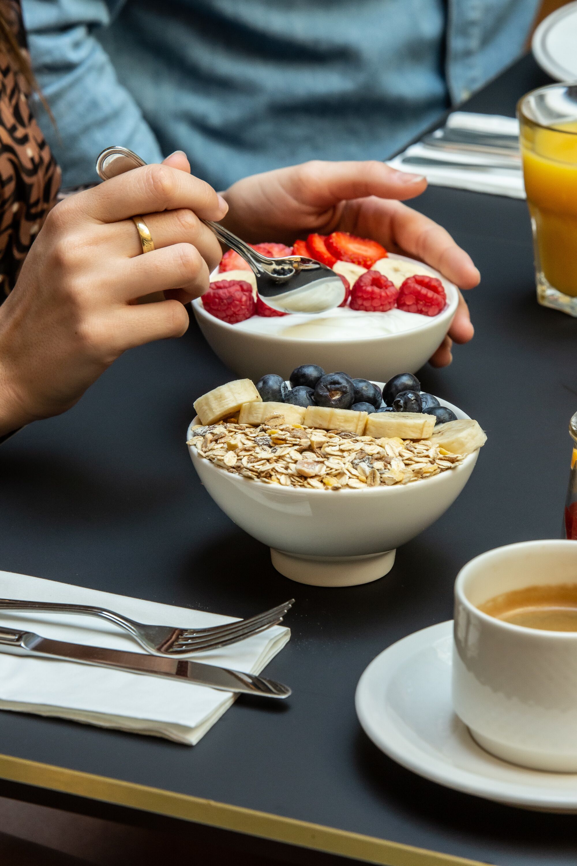 Un desayuno con dos tazones de cereal cubiertos de frutas y una taza de café.