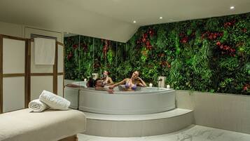 Un espacio de spa con un jacuzzi, una camilla de masaje y una pared decorada con un diseño de hojas verdes.