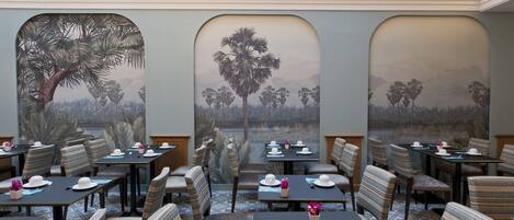 A dining area with tables set for service, featuring a mural of palm trees and a landscape view.