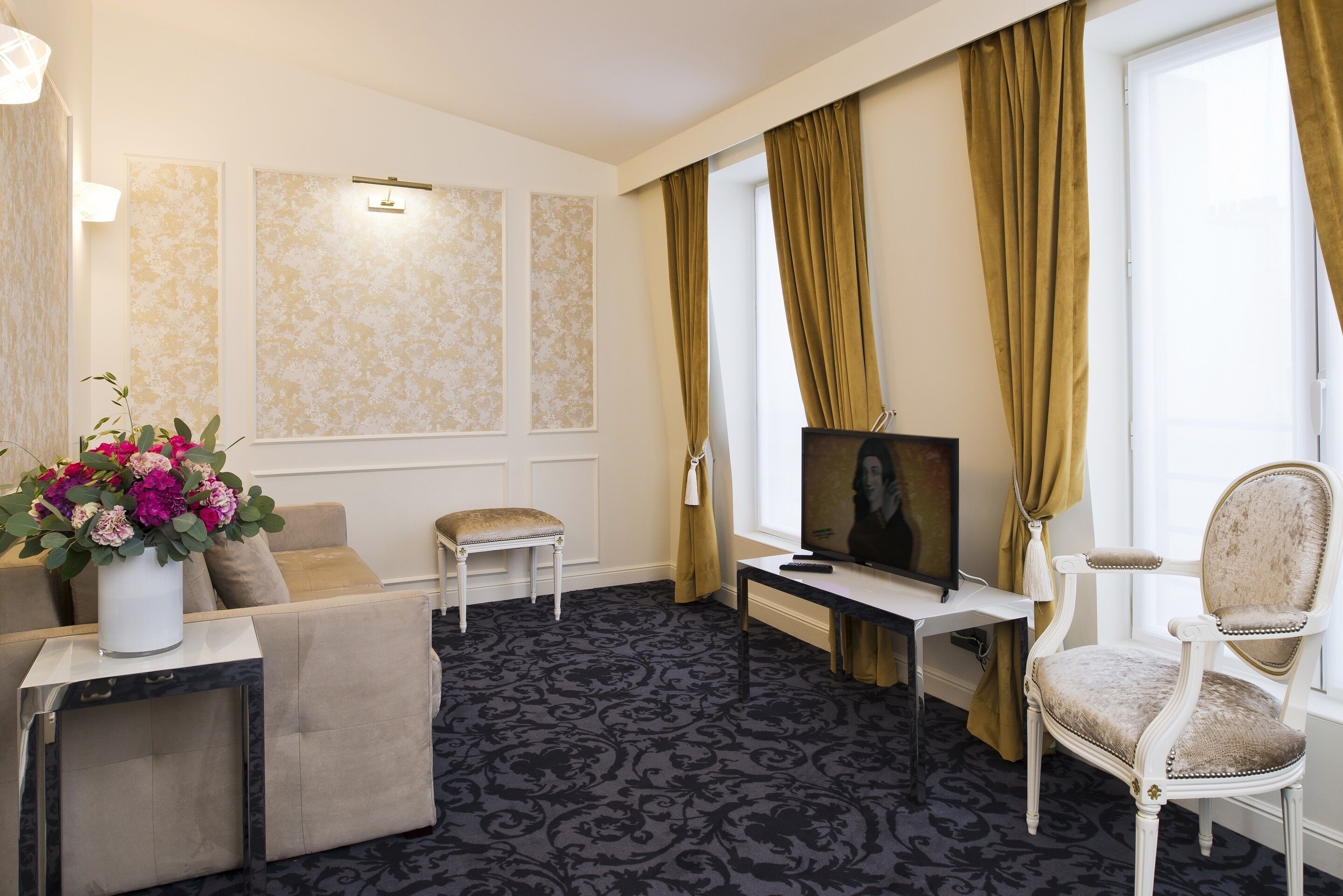 Habitación de hotel con sofá, sillón, televisor y un jarrón decorativo con flores.