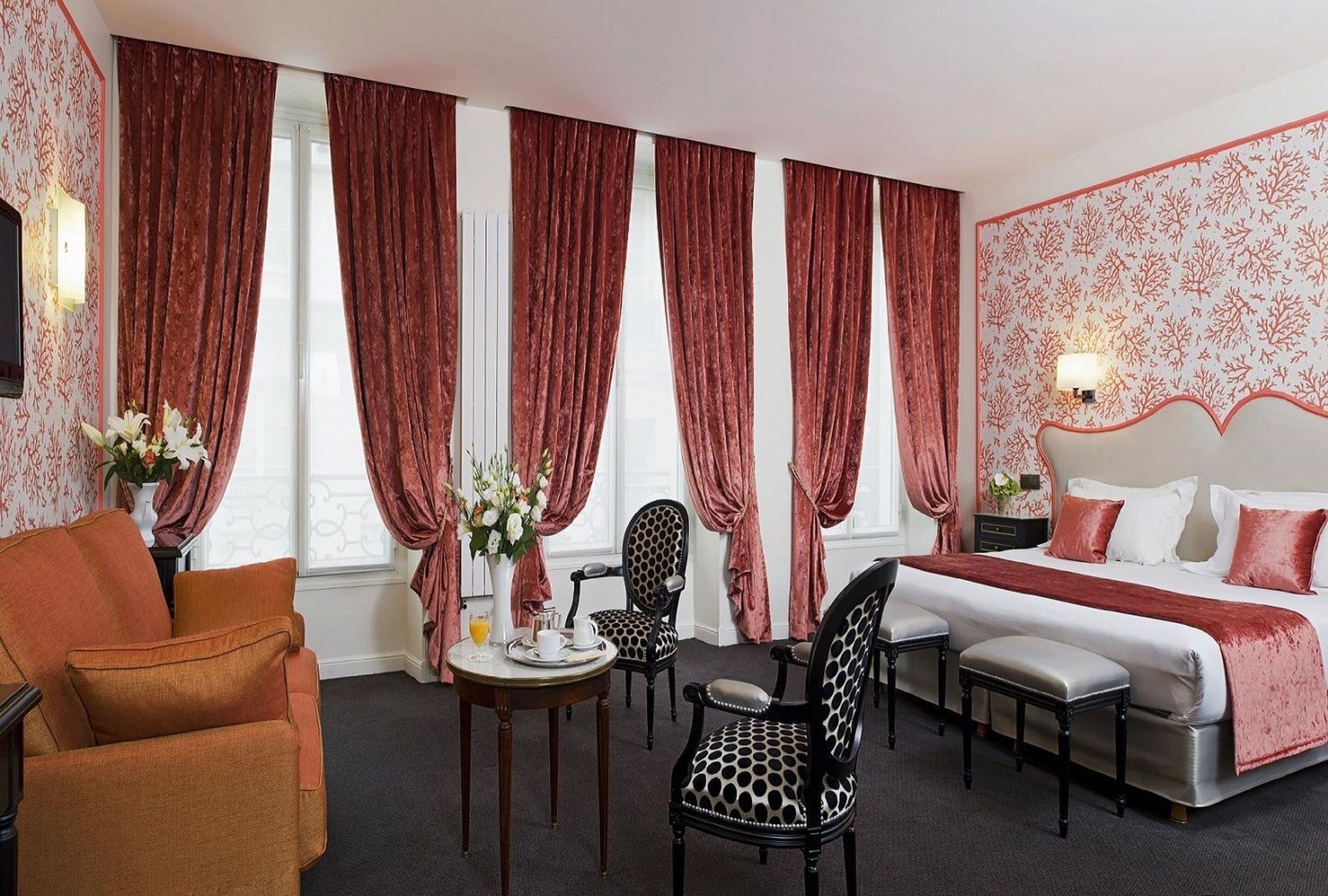 A hotel room with a bed, two chairs, a small table with a vase of flowers, and a sofa.