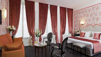 A hotel room with a bed, two chairs, a small table with a vase of flowers, and a sofa.