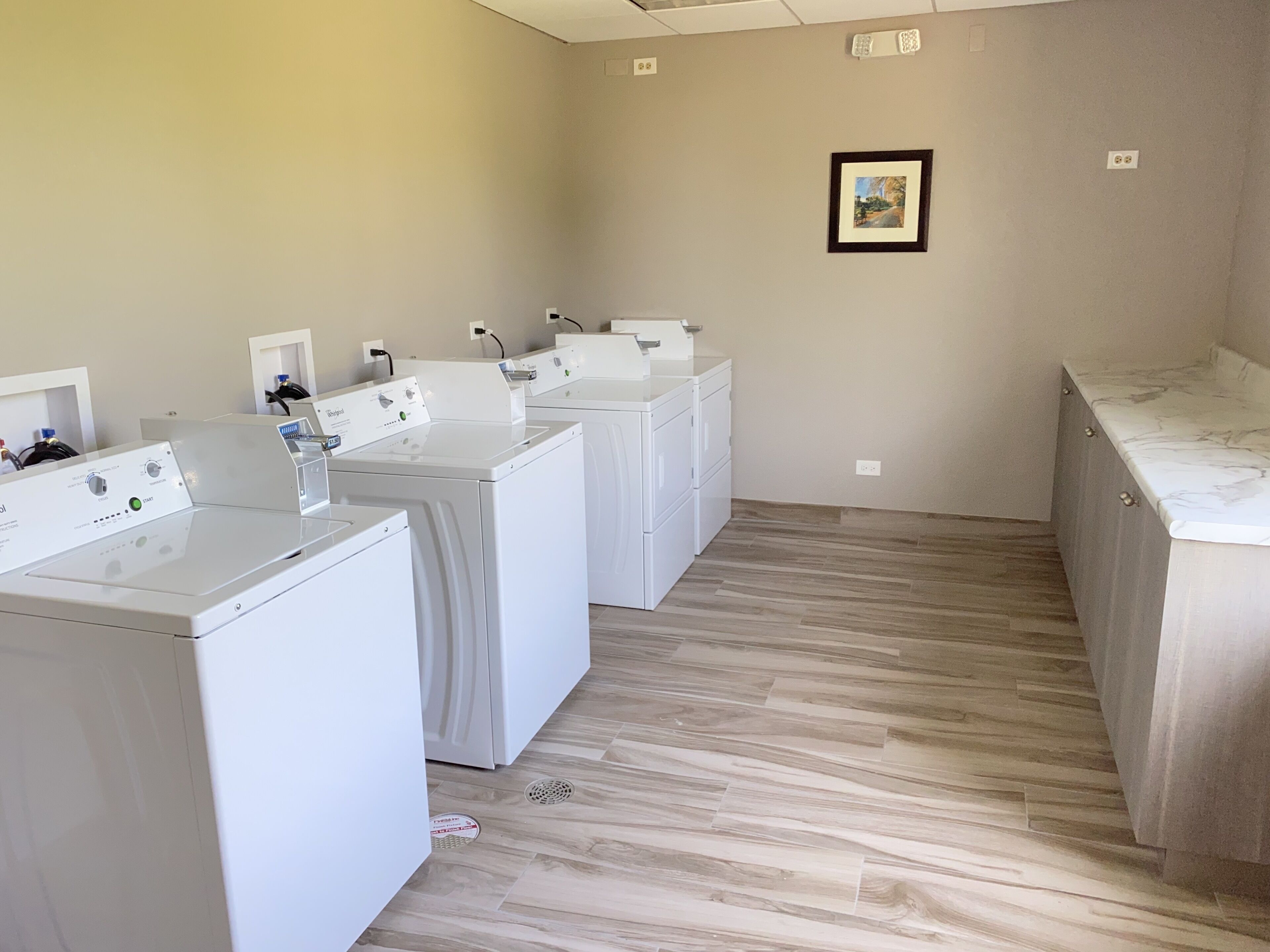 A laundry room with four white washing machines, a sink, and a marble countertop.