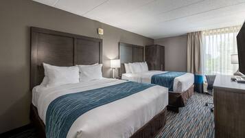 A hotel room with two beds, a desk, and a window with curtains.