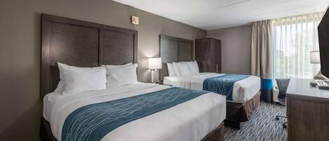 A hotel room with two beds, a desk, and a window with curtains.