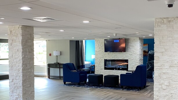 A lobby with a stone column, blue seating, a flat-screen TV, and a fireplace. - Comfort Inn Chicago Schaumburg - O'Hare Airport (Schaumburg)