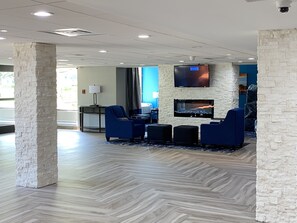 Relax in the stylish lobby, featuring a seating area with armchairs and a coffee table, a flat-screen TV, and a large window with curtains.