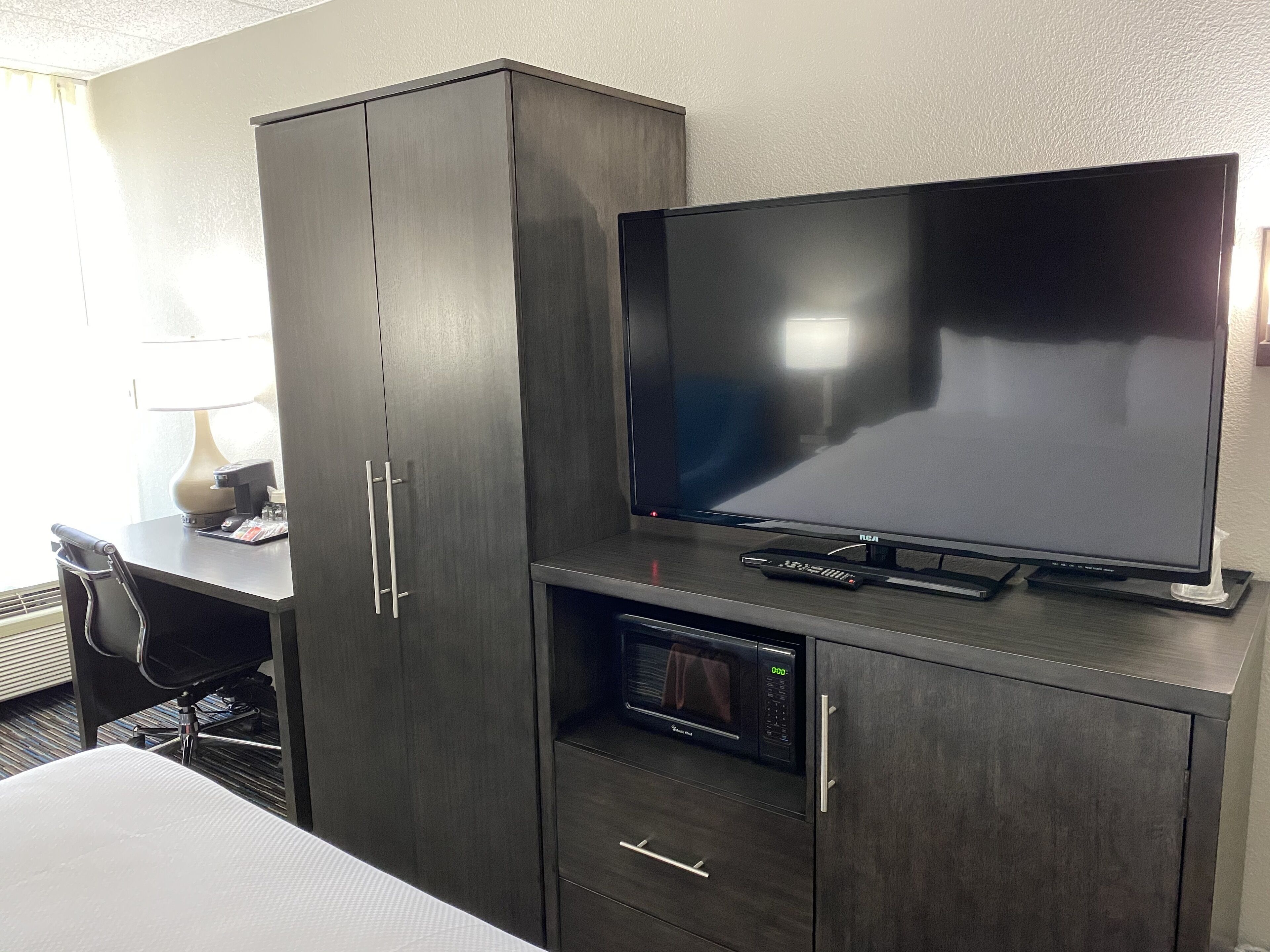 Une chambre d’hôtel équipée d’un grand téléviseur à écran plat, d’un four à micro-ondes, d’un bureau avec une lampe et d’une chaise.