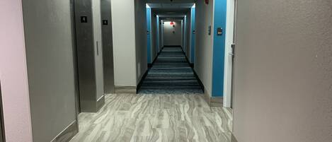 A hotel hallway with a marble floor, blue walls, and numbered doors.