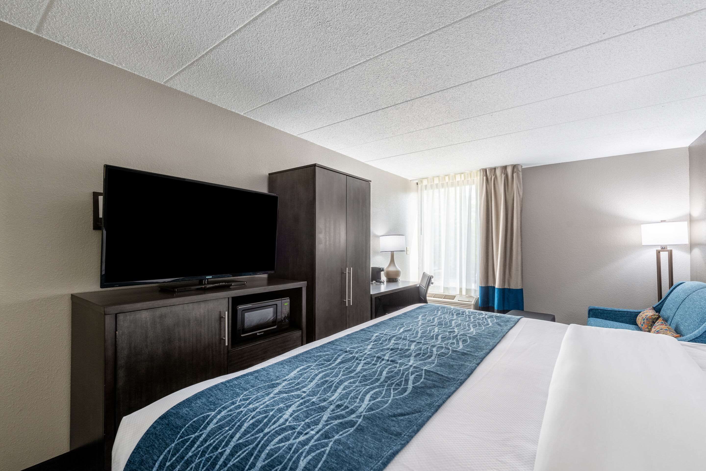 A hotel room with a large bed, a flat-screen TV, a desk with a lamp, and a wardrobe.