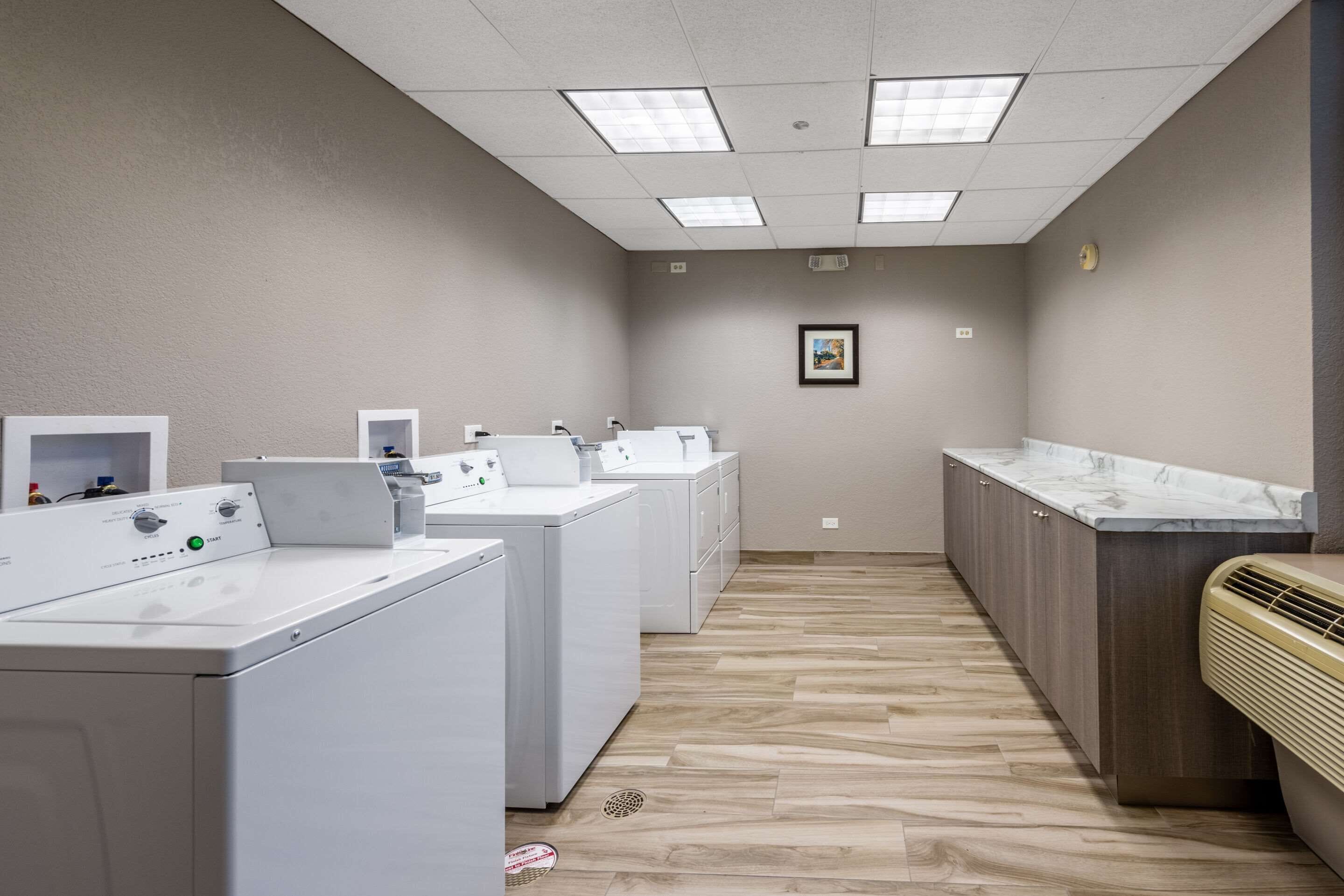A laundry room with multiple washing machines, a drying rack, and a countertop with a sink.