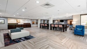 A spacious lobby with a herringbone-patterned floor, a reception desk, a seating area with a sofa and chairs, and a television screen. - Comfort Inn Chicago Schaumburg - O'Hare Airport (Schaumburg)