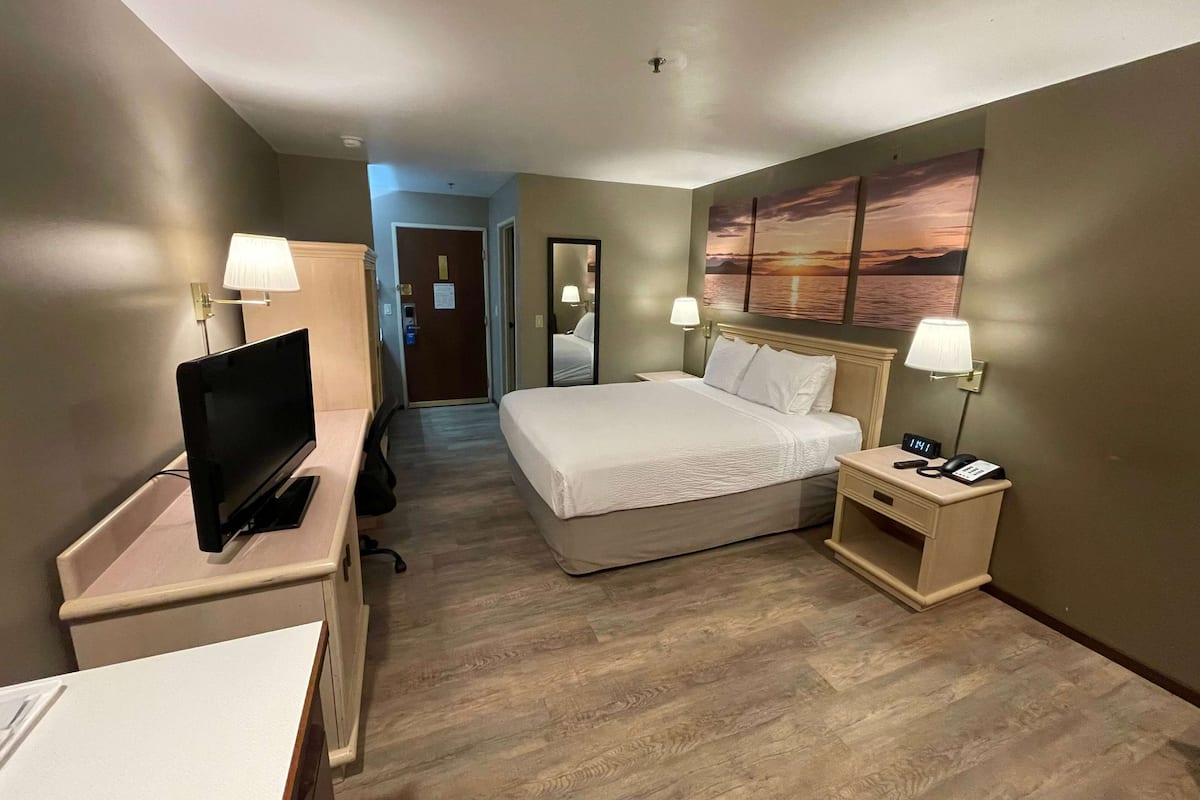A hotel room with a bed, bedside tables, a TV, and a painting on the wall.