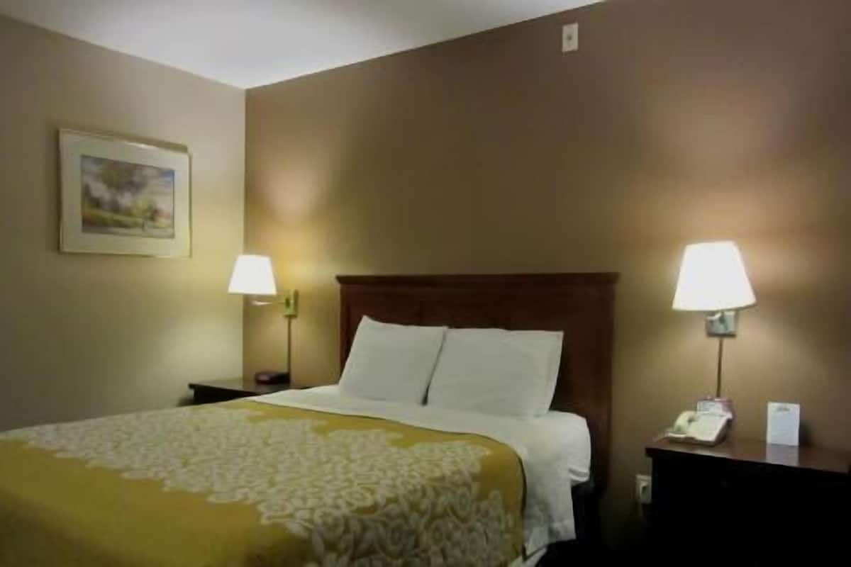 A hotel room with a bed, two bedside lamps, a nightstand, a framed picture on the wall, and a telephone on the nightstand.