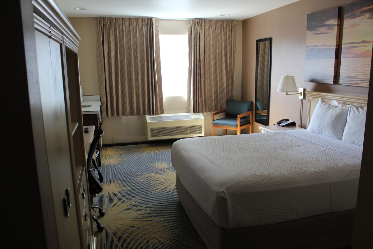 A hotel room with a large bed, a desk, a chair, a desk lamp, and a window with curtains.