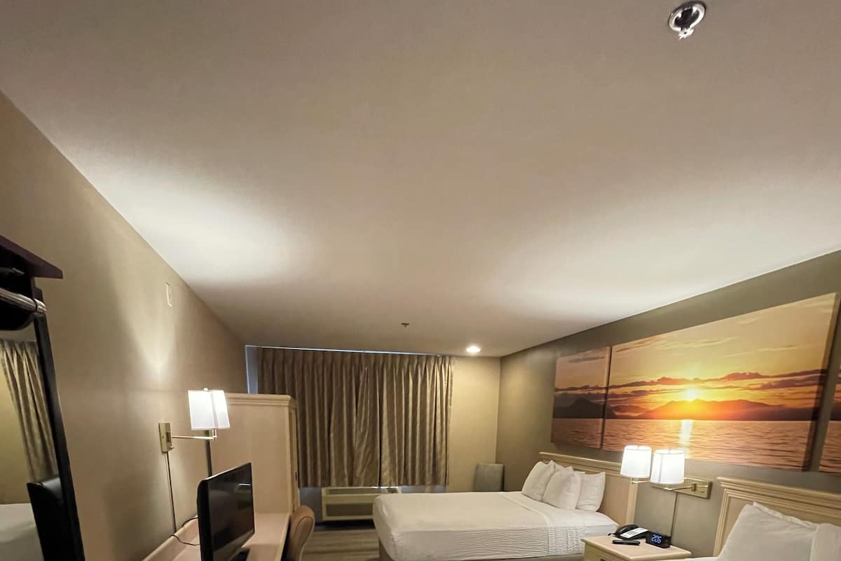 A hotel room with two beds, a desk with a computer, a TV, and a painting of a sunset.
