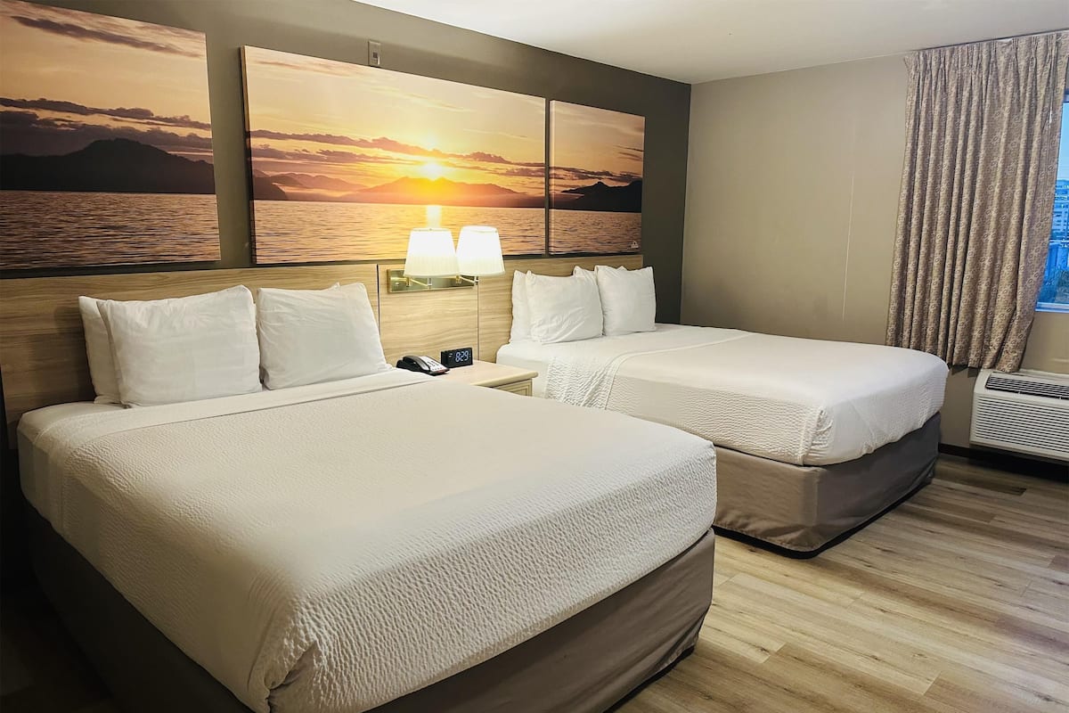 A hotel room with two beds, a nightstand with a lamp, a wall-mounted clock, and a window with curtains.
