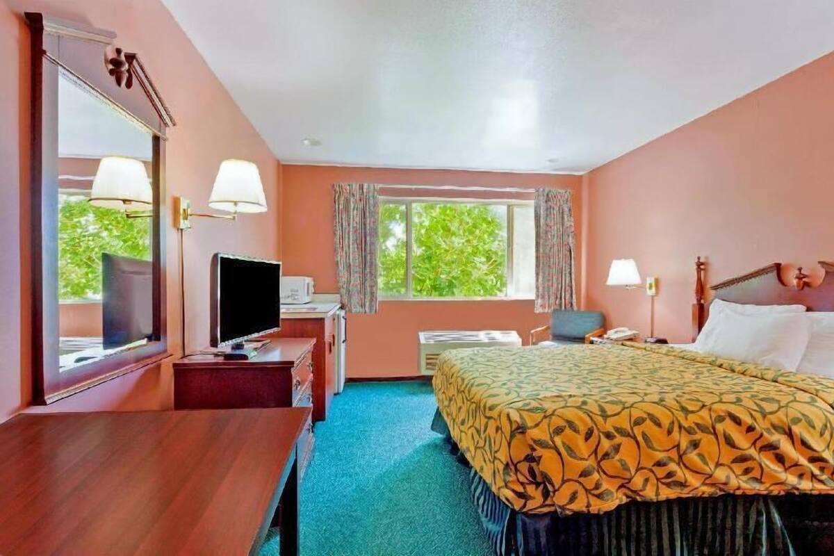 A hotel room with a bed, desk, television, and a window with curtains.